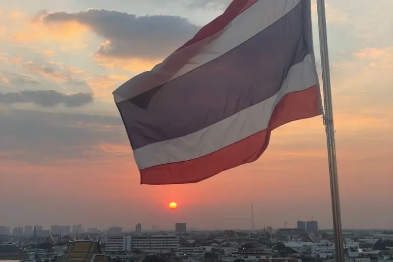 Bandiera della Thailandia che sventola al tramonto sopra lo skyline di Bangkok, vista dalla terrazza panoramica del tempio Wat Saket.