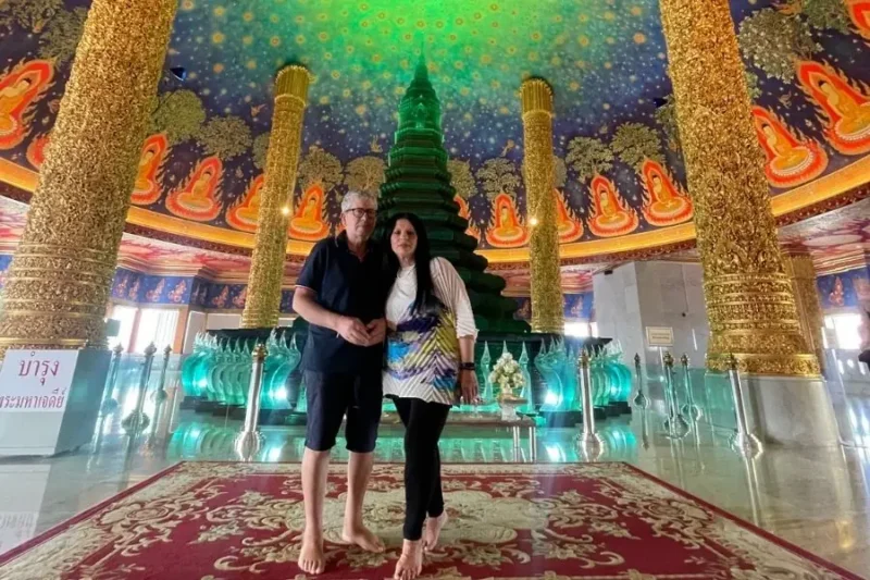 Coppia di turisti all'interno del tempio Wat Paknam Phasi Charoen a Bangkok, davanti alla stupa di vetro verde smeraldo e sotto il soffitto stellato dipinto.