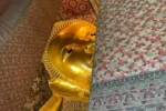 Dettaglio del volto del Buddha Sdraiato (Wat Pho) a Bangkok, statua dorata monumentale tra pilastri decorati con motivi floreali.