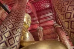 Statua dorata del Buddha in tempio Wat Phanan Choeng Worawihan con mura decorate rosso e oro