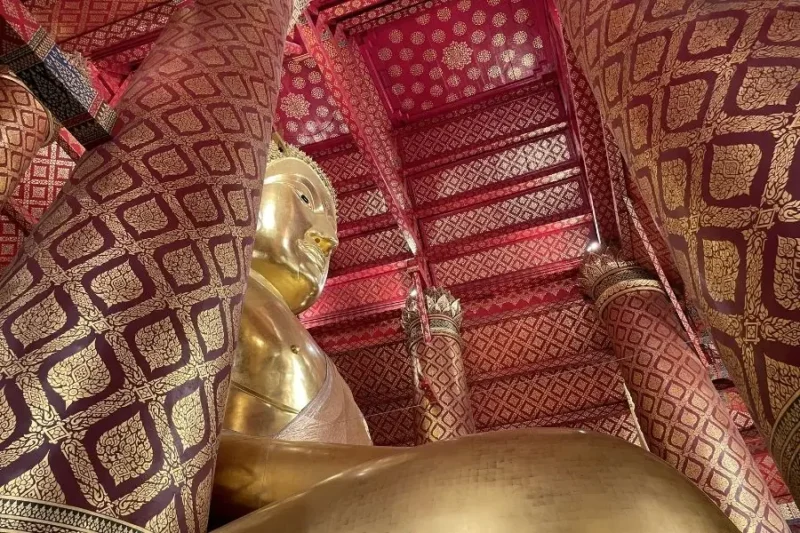 Statua dorata del Buddha in tempio Wat Phanan Choeng Worawihan con mura decorate rosso e oro