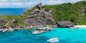 Spiaggia tropicale con acque turchesi e barche vicino a rocce e vegetazione lussureggiante in Similan Island