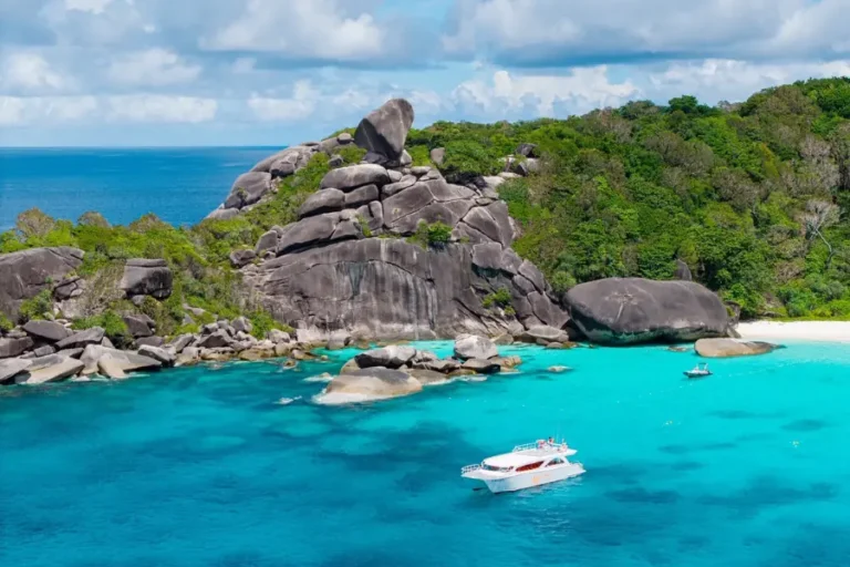 Spiaggia tropicale con acque turchesi e barche vicino a rocce e vegetazione lussureggiante in Similan Island