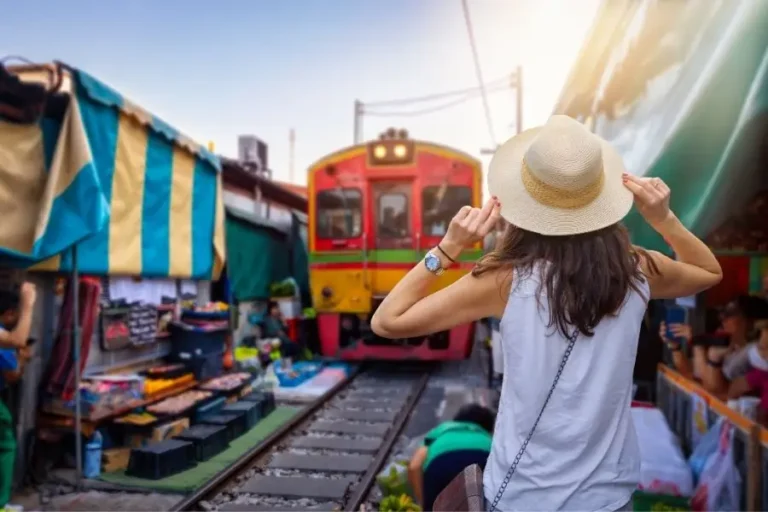 Mercato thailandese con treno in arrivo tra le bancarelle affollate