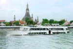 Nave da crociera Grand Pearl in navigazione diurna sul fiume Chao Phraya a Bangkok, con le imponenti guglie del tempio Wat Arun sullo sfondo.