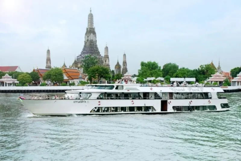 Nave da crociera Grand Pearl in navigazione diurna sul fiume Chao Phraya a Bangkok, con le imponenti guglie del tempio Wat Arun sullo sfondo.