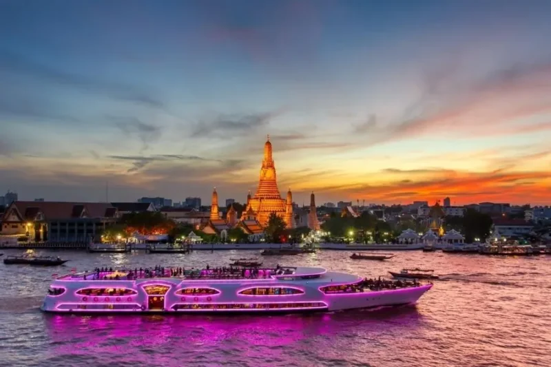 Crociera Wonderful Pearl illuminata di rosa sul fiume Chao Phraya a Bangkok, con il tempio Wat Arun illuminato al tramonto sullo sfondo.