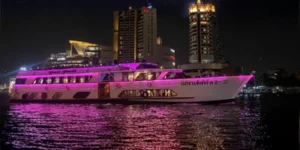 Nave da crociera Grand Pearl 2 illuminata di rosa durante una cena sul fiume Chao Phraya a Bangkok, con lo skyline notturno della città sullo sfondo.