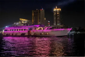 Nave da crociera Grand Pearl 2 illuminata di rosa durante una cena sul fiume Chao Phraya a Bangkok, con lo skyline notturno della città sullo sfondo.