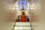 Monaco buddista seduto in meditazione davanti a statua dorata al Wat Saket