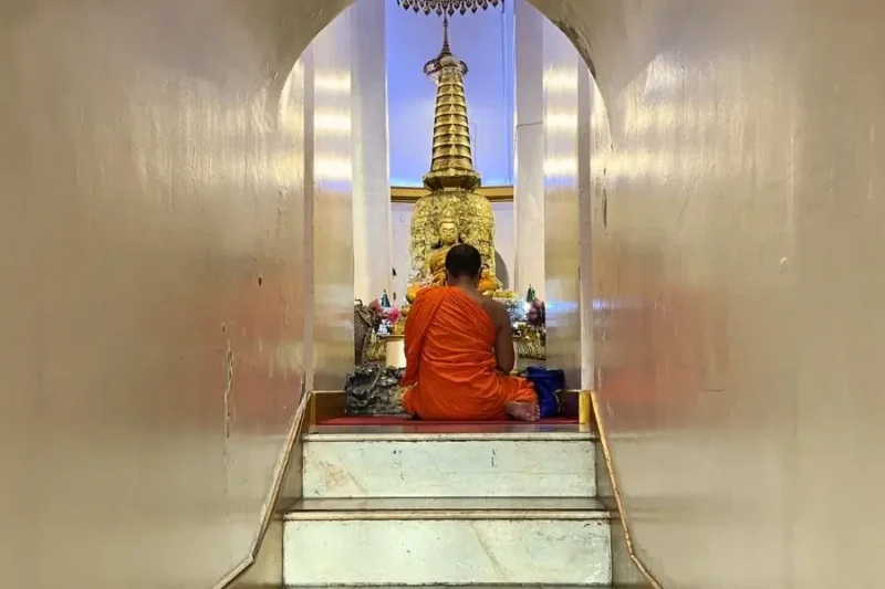 Monaco buddista seduto in meditazione davanti a statua dorata al Wat Saket