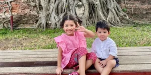 Piccoli Turisti sorridenti posano con sfondo il Buddha incastonato tra le radici del Wat Maha That - Ayutthaya