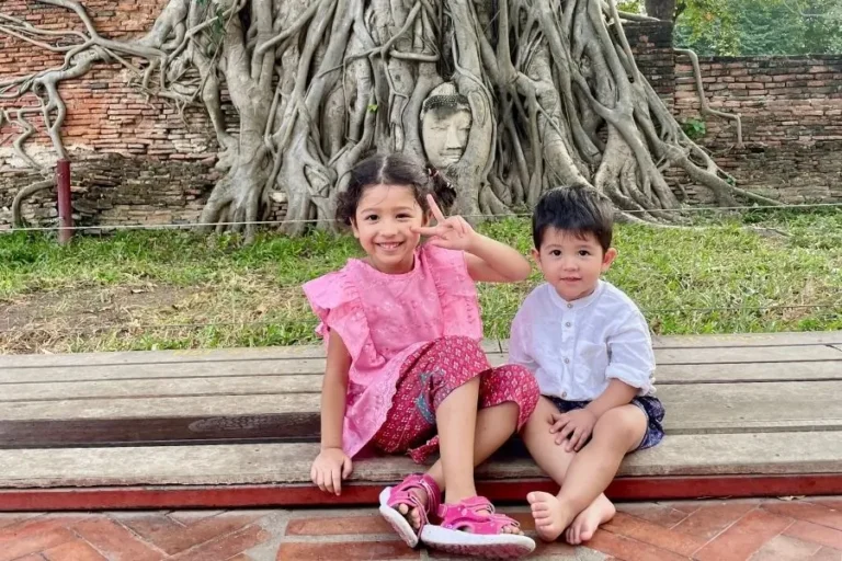 Piccoli Turisti sorridenti posano con sfondo il Buddha incastonato tra le radici del Wat Maha That - Ayutthaya