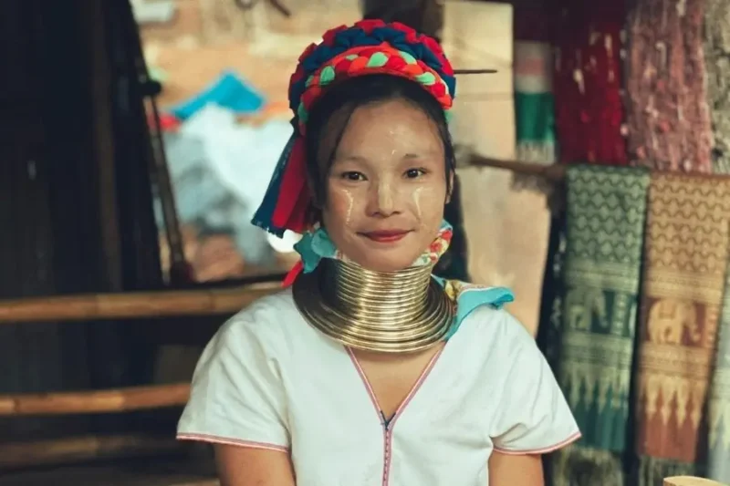 Giovane Donna della tribù Kayan (conosciute come Long Neck) con i tradizionali anelli di ottone al collo, con tessuti colorati sullo sfondo.
