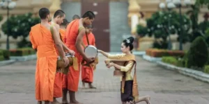 Monaci con abiti arancioni ricevono offerte da una donna inginocchiata in un contesto templare