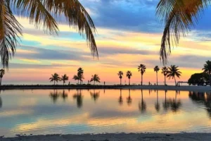 Tramonto tropicale su una spiaggia con palme e riflessi sull'acqua