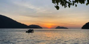 Barca su mare al tramonto tra isole e cielo colorato