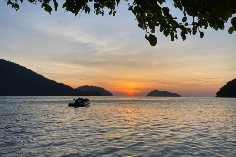 Barca su mare al tramonto tra isole e cielo colorato