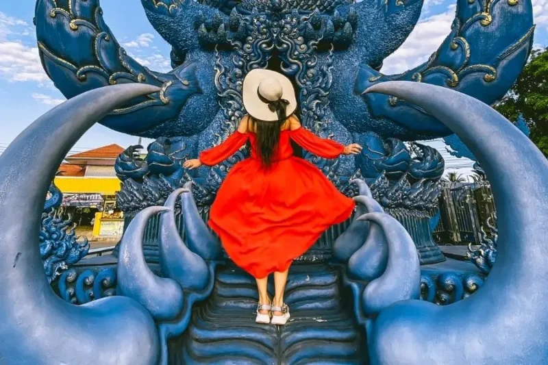 Donna in abito rosso su struttura blu del Tempio Blu in Thailandia