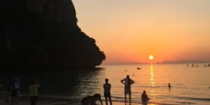 Tramonto su spiaggia tropicale Railay con scogliere e persone in mare