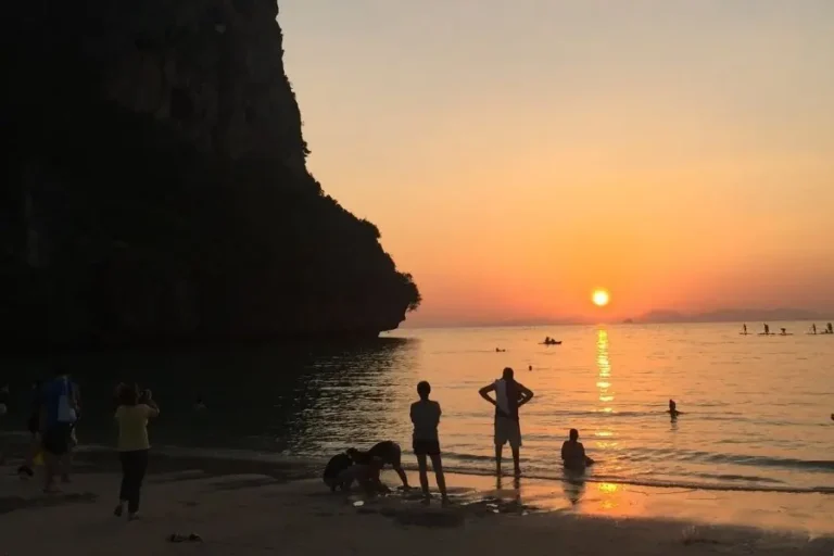 Tramonto su spiaggia tropicale Railay con scogliere e persone in mare