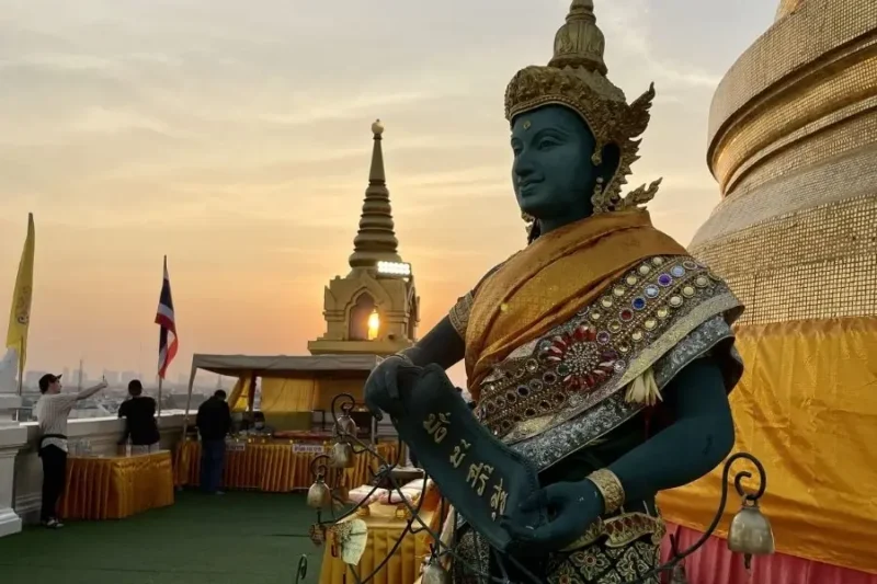 Statua dorata di divinità su terrazza del Wat Saket al tramonto
