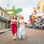Turiste in Giro Per Yorawat 1 I Quartieri di Bangkok: guida completa per scegliere Cosa Visitare e dove dormire Due donne passeggiano in una vivace strada asiatica con tuk-tuk
