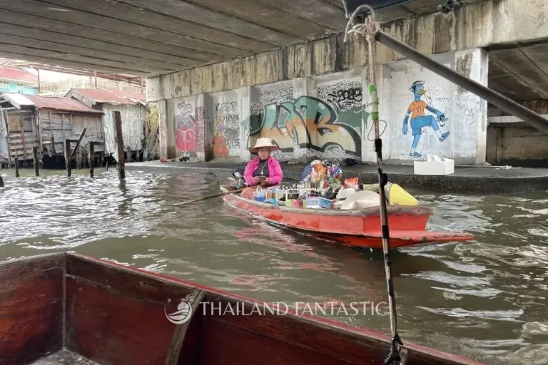 Venditrice su una barca carica di prodotti sotto un ponte, sui canali di Thonburi a Bangkok