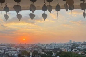 Tramonto panoramico su Bangkok visto dal tempio Wat Saket (Monte d'Oro), con campanelle buddhiste tipiche in primo piano.