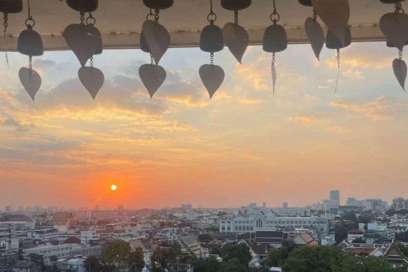 Tramonto panoramico su Bangkok visto dal tempio Wat Saket (Monte d'Oro), con campanelle buddhiste tipiche in primo piano.