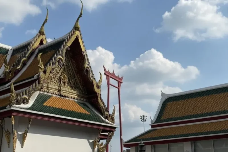 Architettura tradizionale tailandese con tetti decorati e cornici ornate, con sfondo The Giant Swing al Wat Suthat a Bangkok